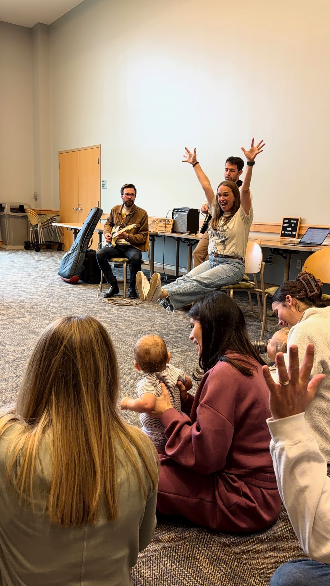 Class leader with arms raised leading a song while a guitarist plays